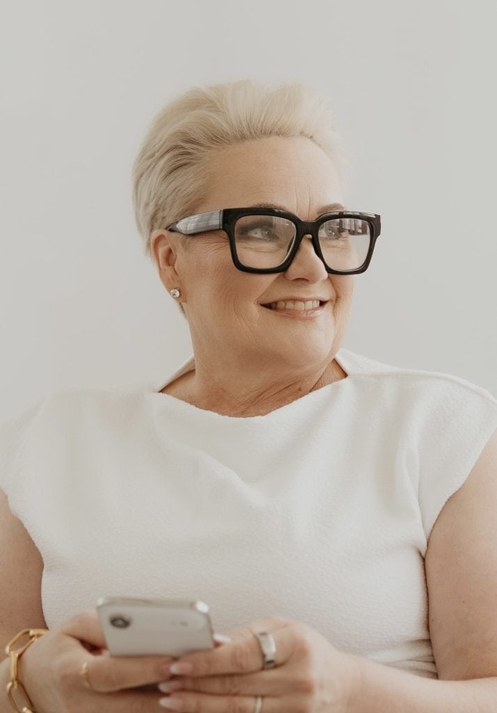 Smiling mature woman with glasses using smartphone for coaching insights.